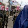 TOPSHOT - Taliban security personnel stand guard as an Afghan burqa-clad woman (R) walks along a street at a market in the Baharak district of Badakhshan province on February 26, 2024. (Photo by Wakil KOHSAR / AFP) (Photo by WAKIL KOHSAR/AFP via Getty Images)