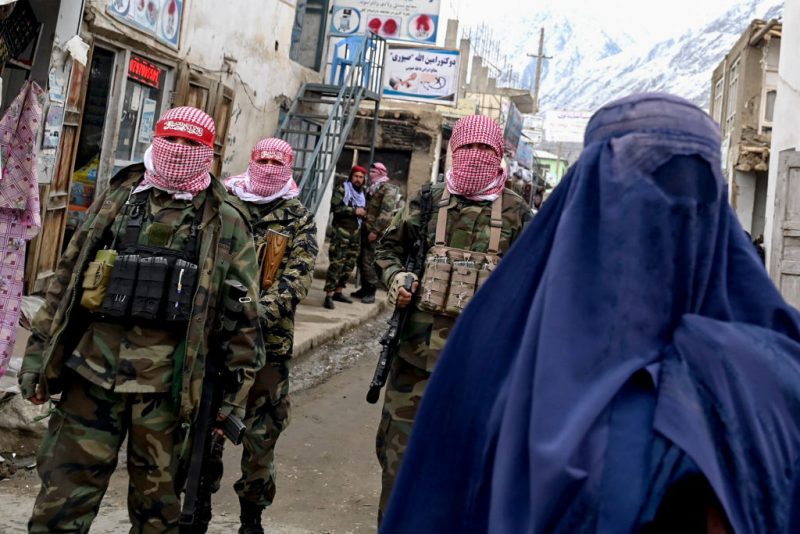 TOPSHOT - Taliban security personnel stand guard as an Afghan burqa-clad woman (R) walks along a street at a market in the Baharak district of Badakhshan province on February 26, 2024. (Photo by Wakil KOHSAR / AFP) (Photo by WAKIL KOHSAR/AFP via Getty Images)