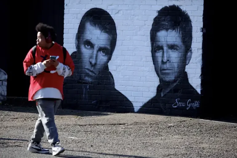 A man walks past a mural of Oasis band members Liam and Noel Gallagher by artist Snow Graffiti on the wall of the Coach and Horses pub in Whitefield, near Manchester, Britain, August 31, 2024. REUTERS/Phil Noble/File Photo