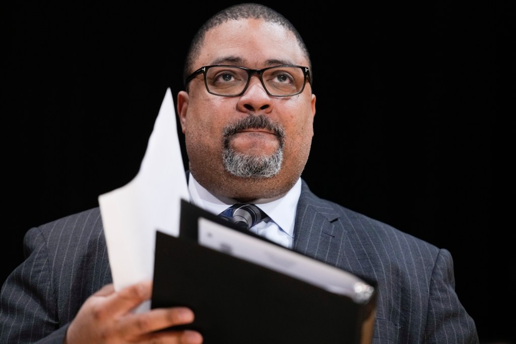 Manhattan District Attorney Alvin Bragg in a suit, holding a folder and papers at a news conference in New York, 2023