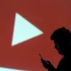 A silhouette of a mobile user is seen next to a screen projection of Youtube logo in this picture illustration taken March 28, 2018. REUTERS/Dado Ruvic/Illustration/ File Photo