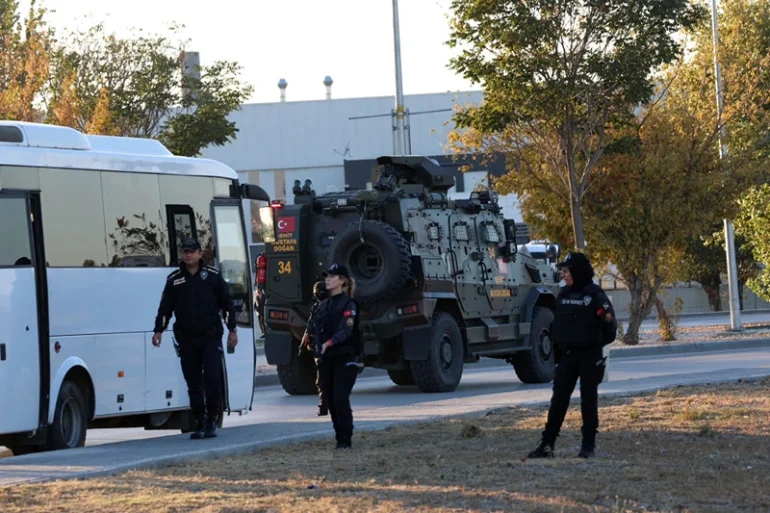 Turkish police officers gather as an armed personnel vehicle drives along a road in Kahramankazan, some 40 kilometers (25 miles) north of Ankara on October 23, 2024, near the gate of the Turkish Aerospace Industries (TAI), after a huge explosion outside the headquarters left a number of people "dead and injured", Turkey's interior minister said, describing it as a "terrorist attack". (Photo by Adem ALTAN / AFP) (Photo by ADEM ALTAN/AFP via Getty Images)