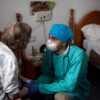 TOPSHOT - Venezuelan doctor Diego Padron holds hands of an isolated resident at an elderly people nursing home in Madrid on April 24, 2020. - What mistakes led to so many deaths? Spain begins to investigate the tragedies behind the closed doors of its retirement homes, where thousands of deaths are attributed to coronavirus. (Photo by OSCAR DEL POZO / AFP) (Photo by OSCAR DEL POZO/AFP via Getty Images)