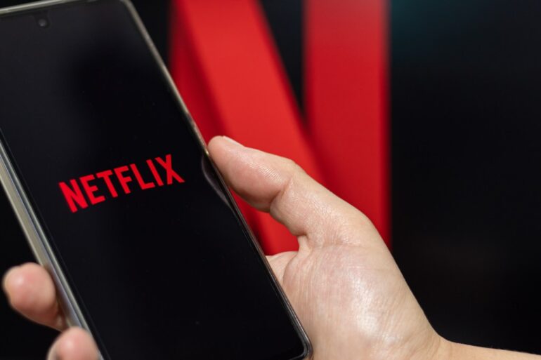 A person opening Netflix on their phone with the Netflix photo in the background.