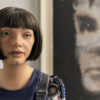 The Ai-Da robot standing in front of her 'AI God' painting on Alan Turing