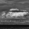 A monochrome image of a distant wind farm with large cloud looming above