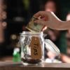 Hand placing dollar bill into a tip jar.