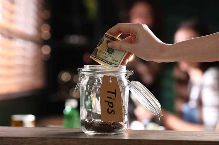 Hand placing dollar bill into a tip jar.