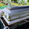 White coffin at a cemetery with flowers nearby.