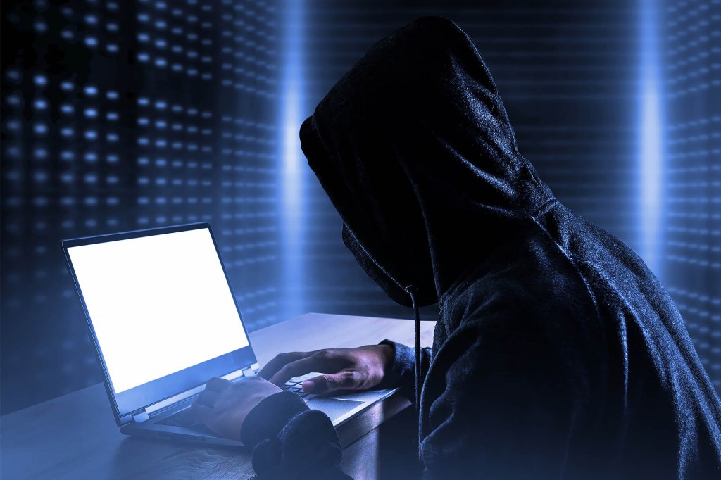 A person in a black hoodie using a laptop, symbolizing a data breach exposing personal information of individuals