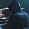 Person in hoodie coding on computer screens.