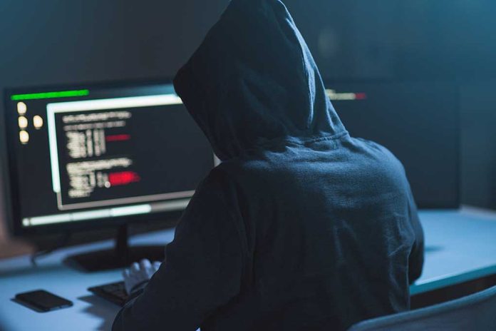 Person in hoodie coding on computer screens.