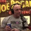 Joe Rogan wearing headphones, holding a can of Bud Light, in his podcast show