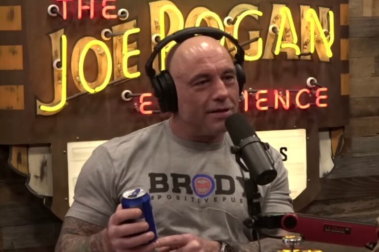 Joe Rogan wearing headphones, holding a can of Bud Light, in his podcast show