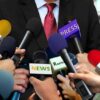 Person surrounded by microphones from various media