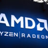 The AMD Logo with the Ryzen and Radeon brand logos underneath on a spotlit wall