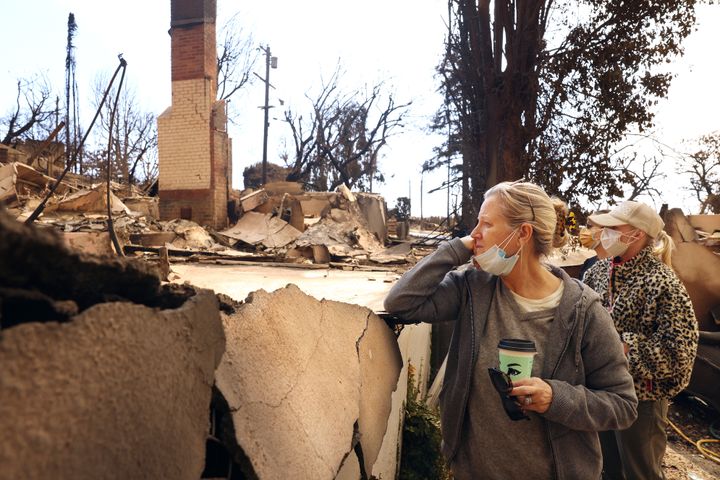 Ana Ashby, front, and her daughters Antonia and Judi, right, take in the destruction of their neighbor's home from the Pacific Palisades Fire.