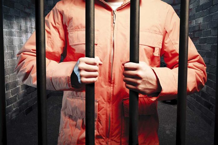 Person in orange jacket behind prison bars.