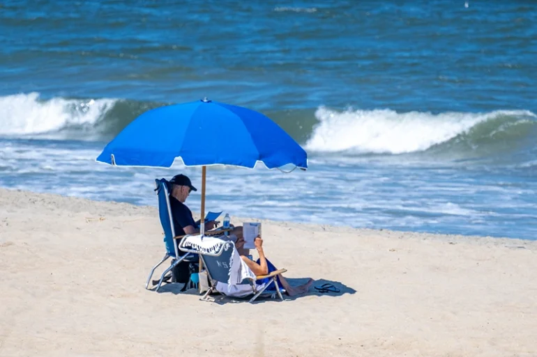 TOPSHOT - US President Joe Biden (L) and US First Lady Jill Biden sit under an umbrella in Rehoboth Beach, Delaware, on July 30, 2023. (Photo by Jim WATSON / AFP) (Photo by JIM WATSON/AFP via Getty Images)