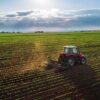 Tractor plowing a vast green field at sunset.