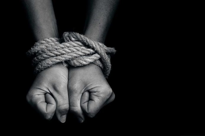 Hands tied with thick rope on black background