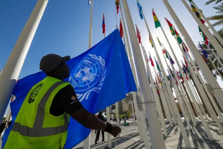 A worker prepares to hoist a United Nations flag with other national flags of participating countries at the venue of the COP28 UN climate summit in Dubai on November 30, 2023. The UN climate conference opens in Dubai on November 30 with nations under pressure to increase the urgency of action on global warming and wean off fossil fuels, amid intense scrutiny of oil-rich hosts UAE. (Photo by Giuseppe CACACE / AFP) (Photo by GIUSEPPE CACACE/AFP via Getty Images)