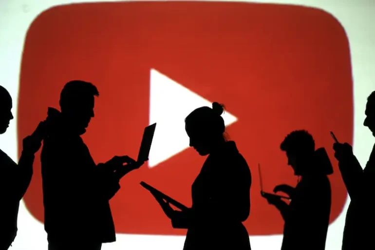 Silhouettes of laptop and mobile device users are seen next to a screen projection of Youtube logo in this picture illustration taken March 28, 2018. REUTERS/Dado Ruvic/Illustration/File Photo