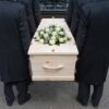 Four people carrying a coffin with white flowers