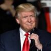 Trump holding microphone wearing suit and red tie