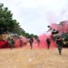 Soldiers running from armored vehicles with red smoke