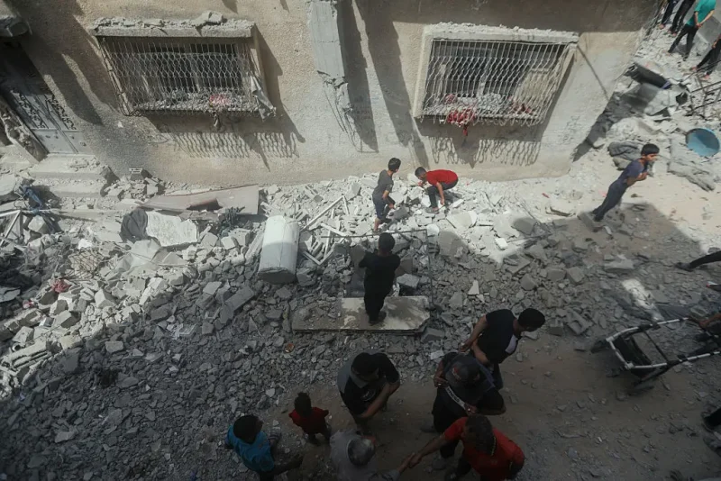 People stand amid rubble and shattered buildings in Gaza City, Palestine, on May 18, 2025. Israeli airstrikes left widespread destruction in residential neighborhoods overnight. (Photo by Youssef Alzanoun / Middle East Images / Middle East Images via AFP) (Photo by YOUSSEF ALZANOUN/Middle East Images/AFP via Getty Images)
