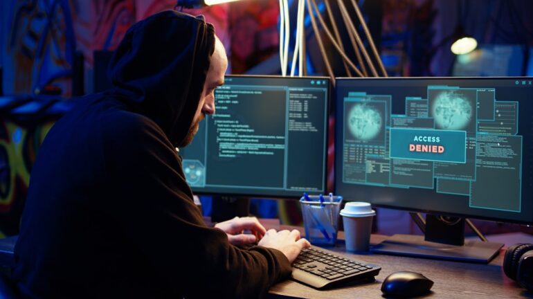 Hacker in dark underground warehouse receiving access denied error message on computer while attempting cyber attack on governmental websites