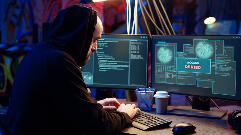 Hacker in dark underground warehouse receiving access denied error message on computer while attempting cyber attack on governmental websites