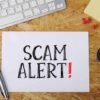 Scam alert message on a wooden desk.