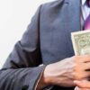 Person in suit putting dollars in jacket pocket