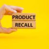 Hand holding Product Recall blocks on yellow background