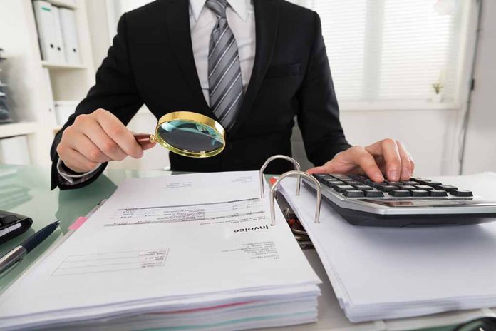 Person examining documents with magnifying glass and calculator.