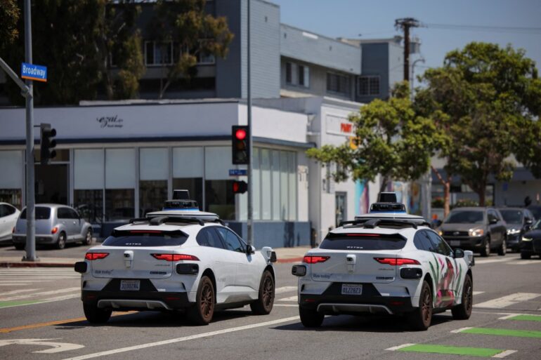Two Waymo self-driving cars stopped at a traffic light.