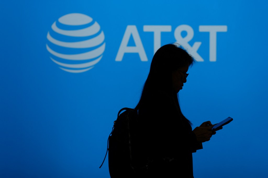 Silhouette of a person using a phone in front of an AT&T logo.
