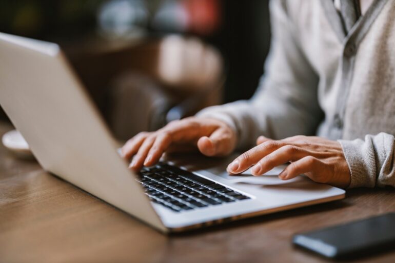 Close-up of hands typing on a laptop in a coffee shop.