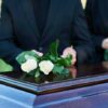 People placing white roses on a casket