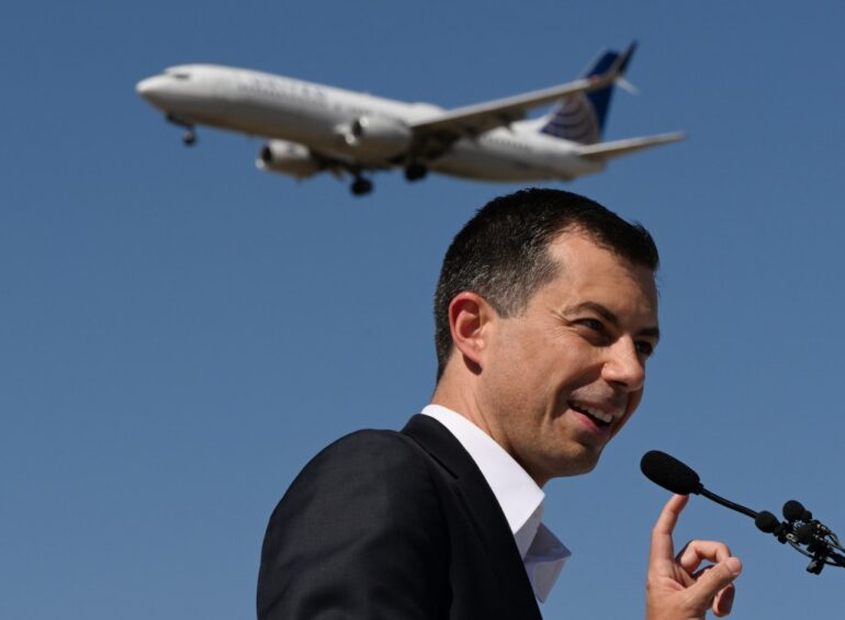 Secretary Pete Buttigieg speaking at Denver International Airport with a plane in the background.