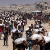 TOPSHOT - People walk with sacks of flour delivered after trucks carrying humanitarian aid entered northern Gaza on July 27, 2025 coming from the Zikim border crossing. (Photo by BASHAR TALEB / AFP) (Photo by BASHAR TALEB/AFP via Getty Images)