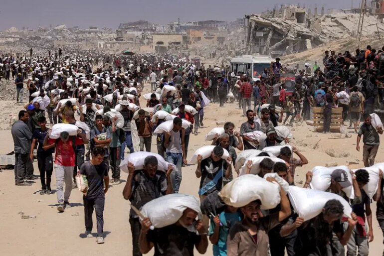 TOPSHOT - People walk with sacks of flour delivered after trucks carrying humanitarian aid entered northern Gaza on July 27, 2025 coming from the Zikim border crossing. (Photo by BASHAR TALEB / AFP) (Photo by BASHAR TALEB/AFP via Getty Images)