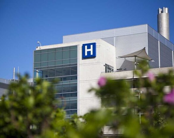 Modern hospital building with a prominent H sign against a clear blue sky