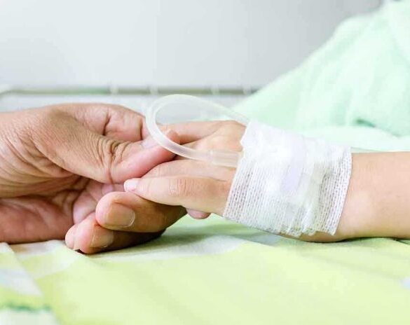 A person holding the hand of a patient with an IV in a hospital bed