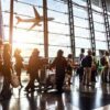 Crowd of travelers in airport terminal with airplane outside.