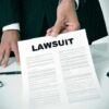 Person holding a document titled LAWSUIT in office.