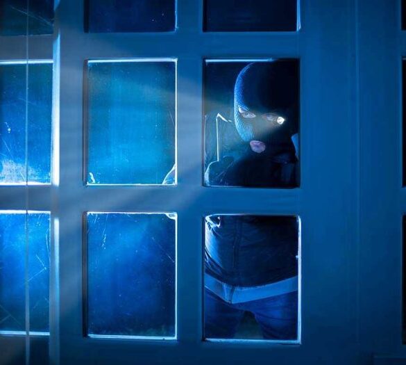 Masked figure peering through glass door at night.