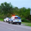 Police car with flashing lights pulling over a white vehicle beside a speed limit sign